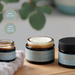 Three jars of MAYDI+ rejuvenating night cream on a wooden surface with greenery in the background.