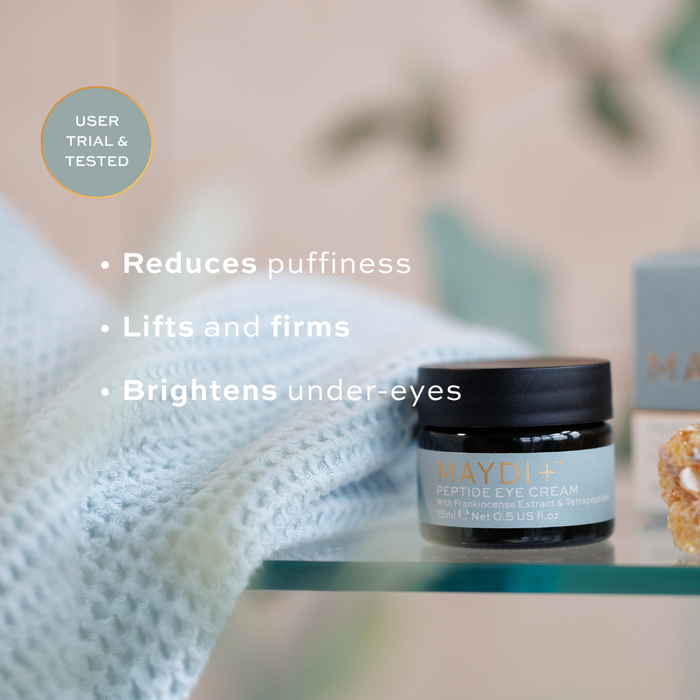 Maydi+ eye cream jar with product benefits text on a blurred background. reduces puffiness, lifts and firms, brightens under-eyes.